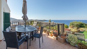 Eine Terrasse mit Tisch und Stühlen, einem Blumentopf und Blick aufs Meer.