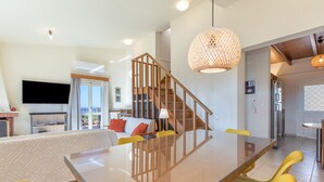 Ein modernes Wohnzimmer mit einem Glastisch, gelben Stühlen, einer Holztreppe und einer großen, gewebten Leuchte.