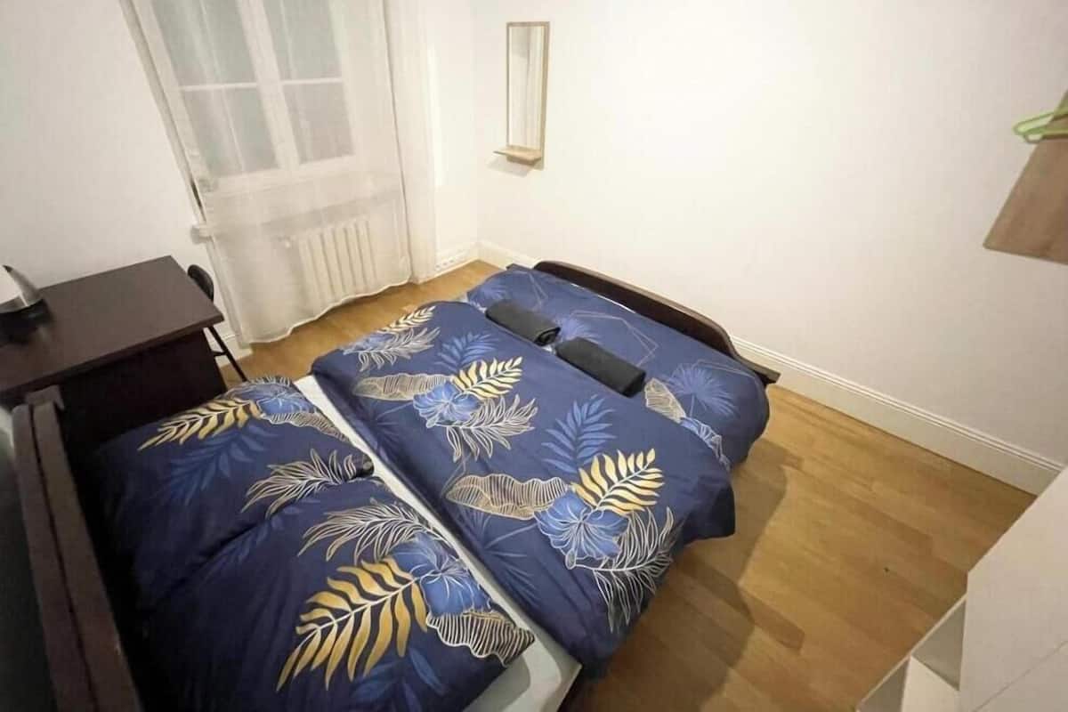 A small room with two single beds, a desk, a chair, a radiator, and a mirror on the wall.
