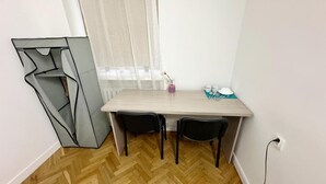 Una habitación pequeña y moderna con suelo de madera tipo espiga, pared blanca sencilla, un escritorio de madera con dos sillas negras y una mesita con un florero y tazas.