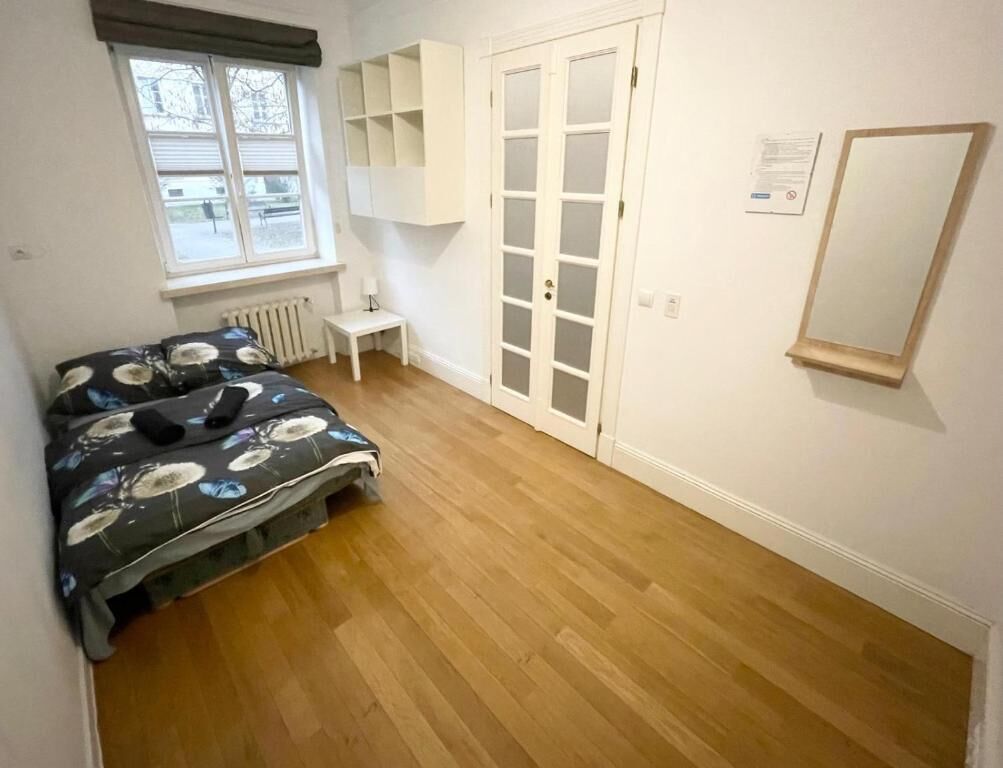 A bedroom with a bed, a radiator, a white wardrobe, a window, and a mirror on the wall.
