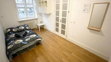A bedroom with a bed, a radiator, a white wardrobe, a window, and a mirror on the wall.