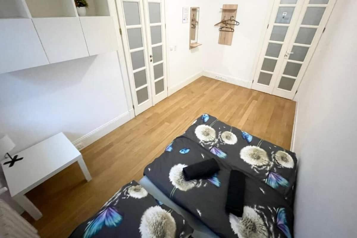A small, compact room with a bed, a white desk, and a wardrobe with frosted glass doors.