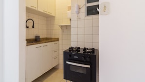 Una cocina compacta con armarios blancos, estufa a gas y horno empotrado.