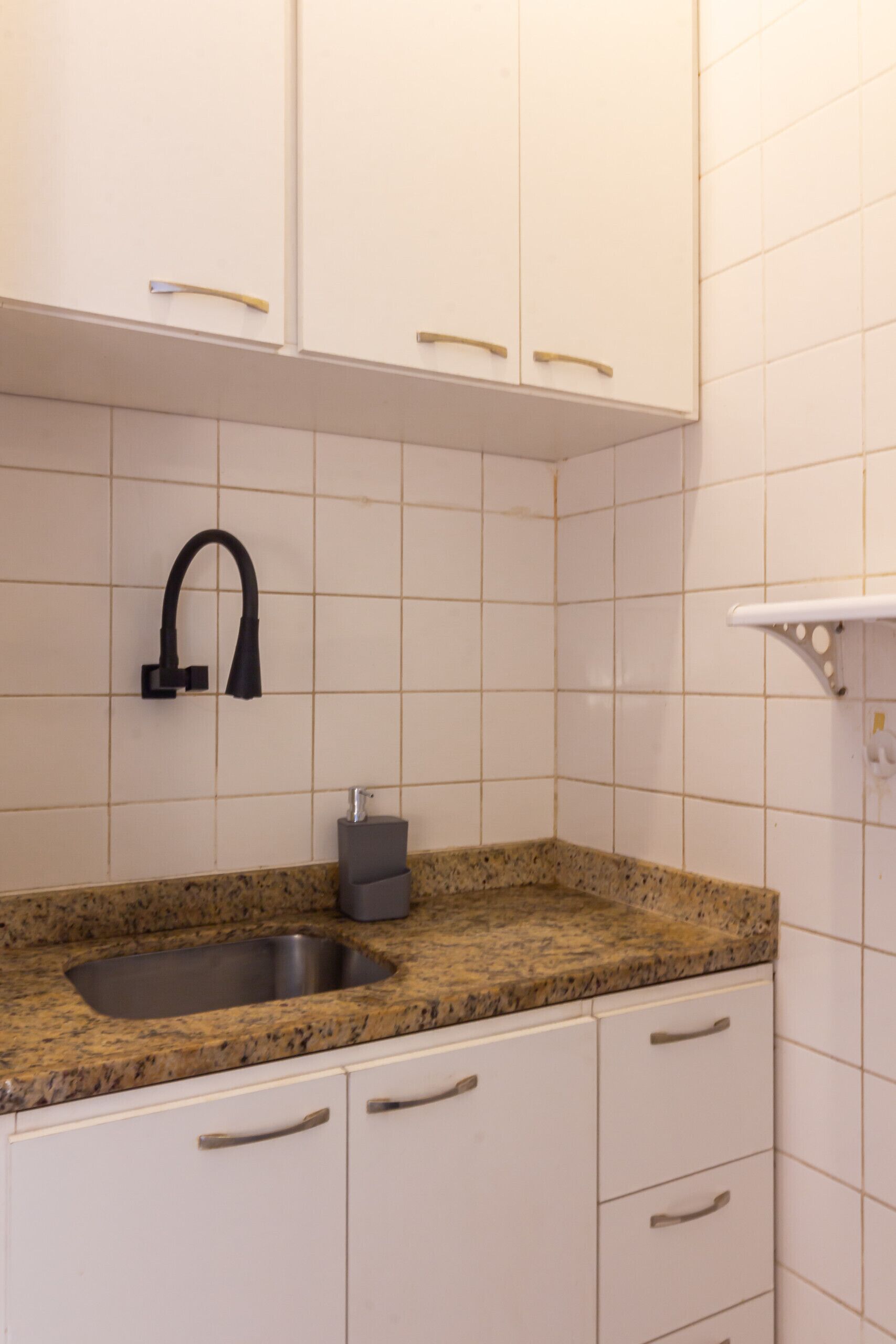 A kitchen with white cabinets, a granite countertop, a stainless steel sink, and a black faucet.
