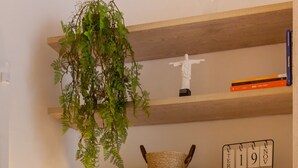 Una habitación con estantes de madera, una planta colgante, una estatua, un calendario, una lámpara y libros.