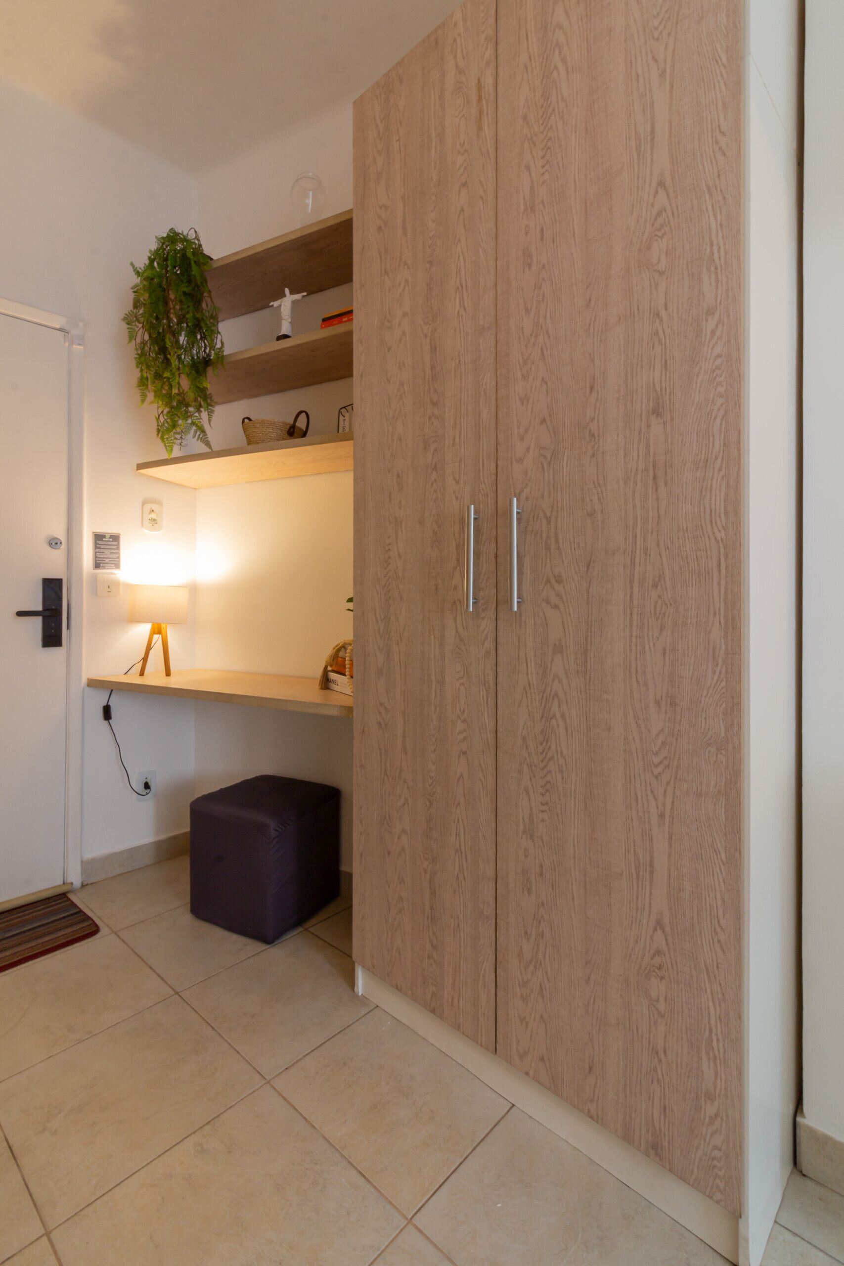 A modern room with a wooden wardrobe, a small desk with a lamp, and a potted plant.