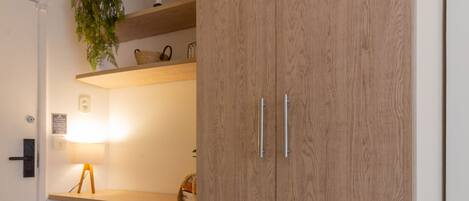Een moderne kamer met een houten garderobe, een klein bureau met een lamp en een potplante.