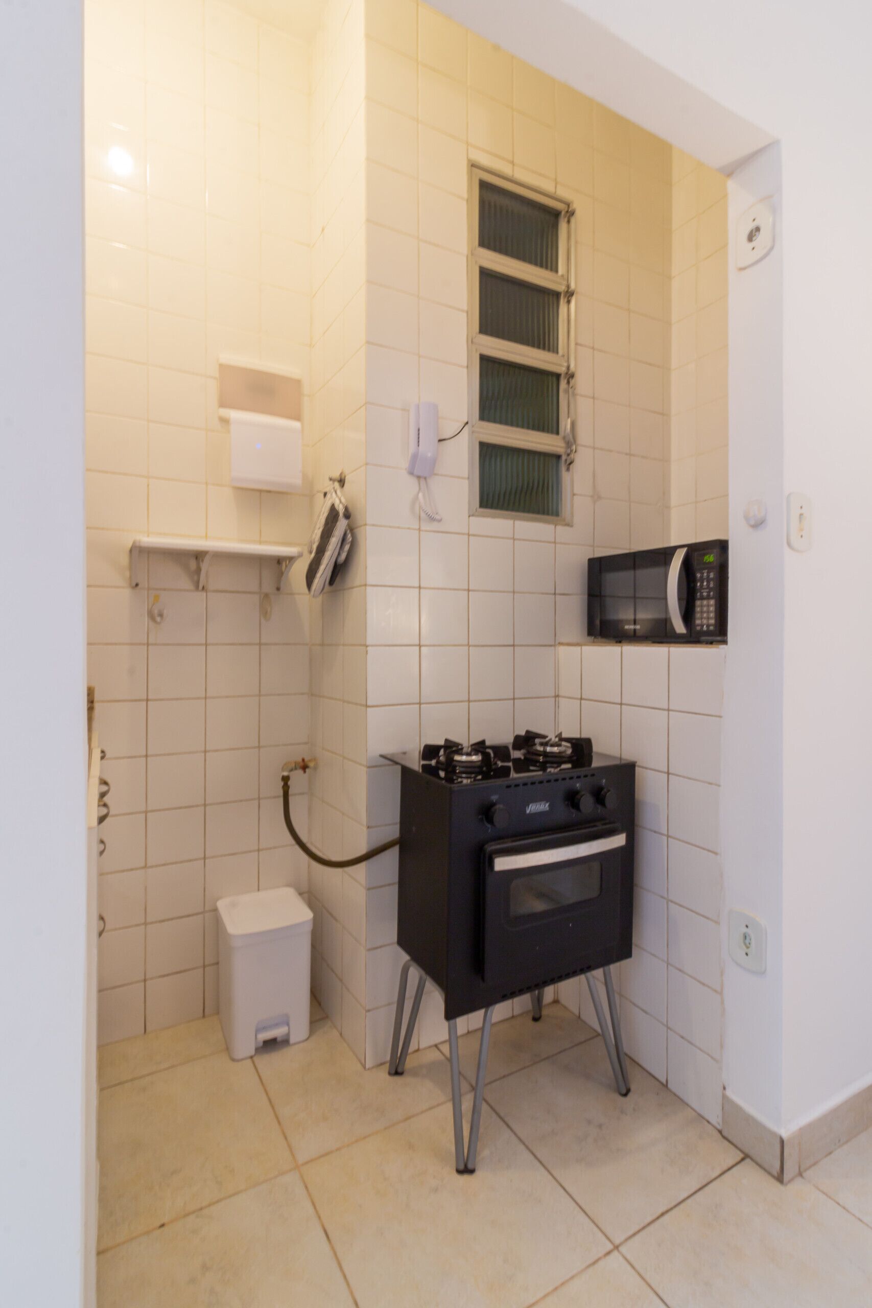 A compact kitchen with a gas stove, microwave, and a small trash bin.