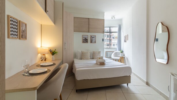 Una habitación de hotel moderna con cama, mesita de noche, lámpara y vistas a la ciudad.