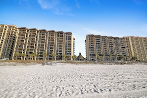A beachfront hotel with multiple floors, balconies, and palm trees. - Romar House 601A by Liquid Life (Orange Beach)