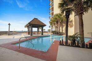 A swimming pool with a gazebo, palm trees, and a building with balconies. - Romar House 601A by Liquid Life (Orange Beach)