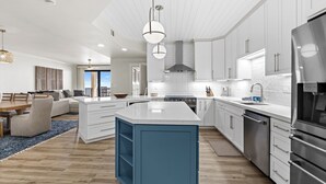 A modern kitchen with white cabinets, a blue island, stainless steel appliances, and a herringbone tile backsplash. - Romar House 601A by Liquid Life (Orange Beach)