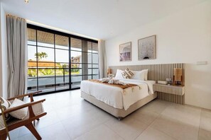 Ein modernes Hotelzimmer mit einem großen Bett, einem Nachttisch, einem Sessel und Blick ins Freie.