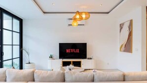 Een moderne woonkamer met een grote flatscreentelevisie, een bank en een hanglamp.