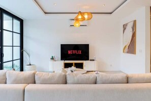 Ein modernes Wohnzimmer mit großem Flachbildfernseher, einer Couch und einer Pendelleuchte.