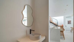 Een moderne badkamer met een minimalistisch ontwerp, met een ronde wasbak en een bijzondere spiegel bevestigd aan de muur.