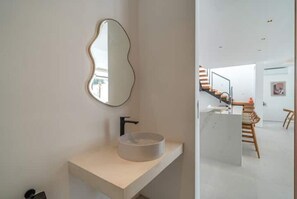 Ein modernes Badezimmer mit minimalistischem Design, das ein rundes Waschbecken und einen einzigartigen, an der Wand montierten Spiegel zeigt.