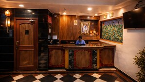 A hotel reception area with a check-in counter, wooden cabinets, a framed picture, and a tiled floor. - Hotel Raja Kalyan (Kalyan)