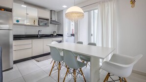 A modern kitchen with white cabinets, a white dining table, and grey chairs. - Apt w/ Barbecue Grill 750m From the Beach Evp0504 (Itapema)