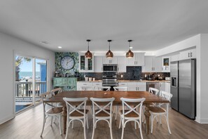 A modern kitchen with white cabinetry, a wooden dining table, and a view of the ocean. - 10BR Family Retreat w/ Private Hot Tub & Beach Access (Garden City Beach)