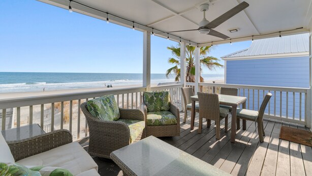 Une terrasse extérieure couverte, aménagée avec des meubles en osier, une table et offrant une vue sur la plage et l’océan.