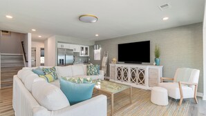 Un salon moderne avec un canapé, un pouf et un téléviseur à écran plat posé sur un meuble.