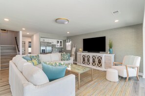 A modern living room with a sofa, ottoman, and a flat-screen TV on a cabinet.