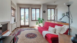A living room with a red sofa, a TV, a lamp, and a large window with a view of mountains. - Terrazza Rooftop (Como)