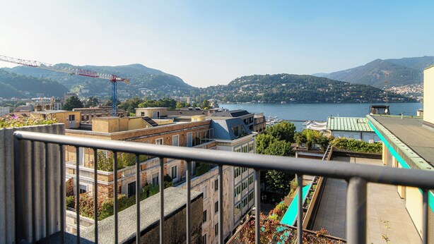 A balcony with a view of a lake, buildings, and mountains. - Terrazza Rooftop (Como)