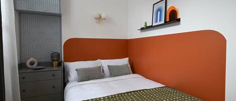 Un dormitorio ordenado con una cama, una mesita de noche, un estante empotrado con adornos y un panel de pared con diseño.