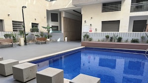 A swimming pool with a tiled deck, surrounded by potted plants and benches.
