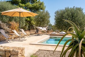 Ein Poolbereich mit Liegestühlen, einer Hängematte und einem Sonnenschirm.