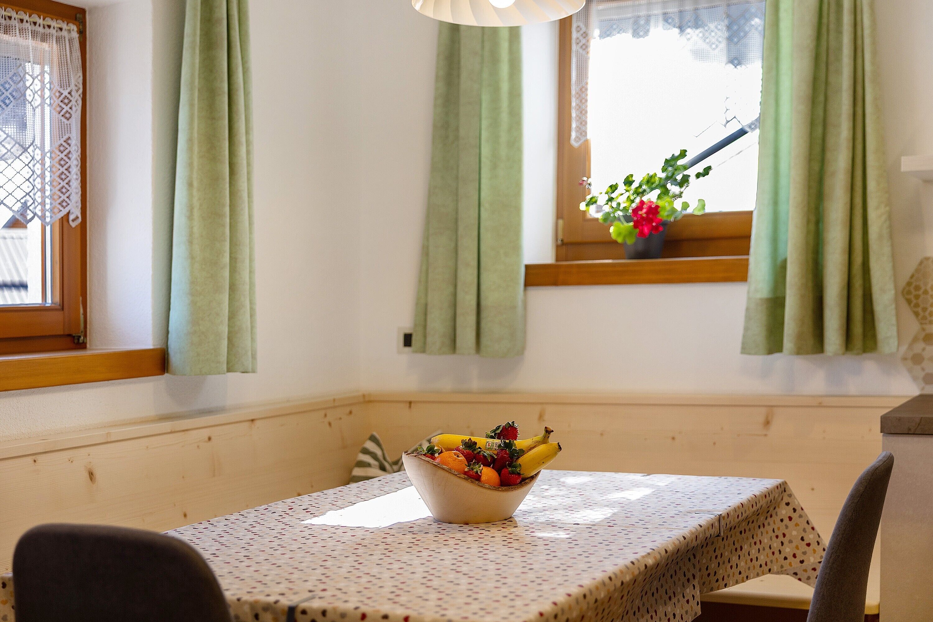 Un coin repas avec une table, des chaises, un saladier de fruits et une fenêtre avec des rideaux.