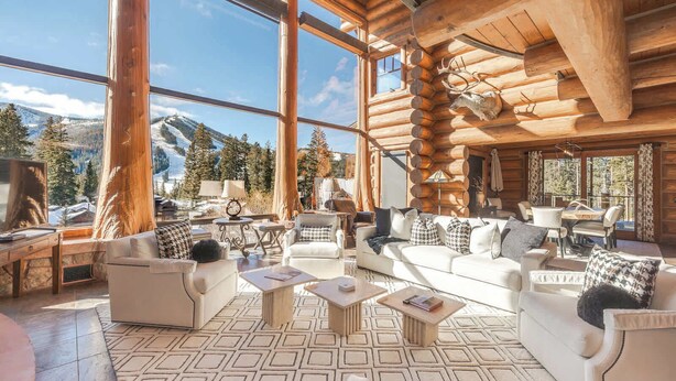 A log cabin interior with a large window offering a mountain view, furnished with white sofas and a dining area. - Forest Setting | Near Trail Access (Winter Park)