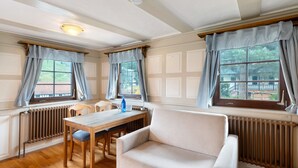 A room with a wooden table, a beige sofa, and two windows with checkered curtains. - Room “Buche” with Shared Garden and Wi-Fi (Sasbachwalden)
