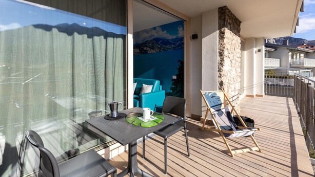 Un balcón con una mesa, sillas, un caballete y vistas a montañas a través de una ventana.