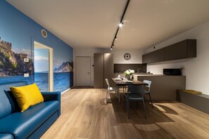 Un soggiorno moderno con un divano blu, un'area pranzo con tavolo e sedie, una cucina con mobili e un'ampia finestra con vista panoramica.