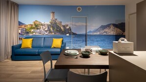 Una habitación con un amplio mural decorativo, un sofá azul con cojines amarillos, una mesa de madera con platos y tazones, y un kit de bienvenida sobre la mesa.