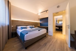 Ein modernes Schlafzimmer mit Bett, Nachttischen, einem integrierten Fernseher und einem begehbaren Kleiderschrank.