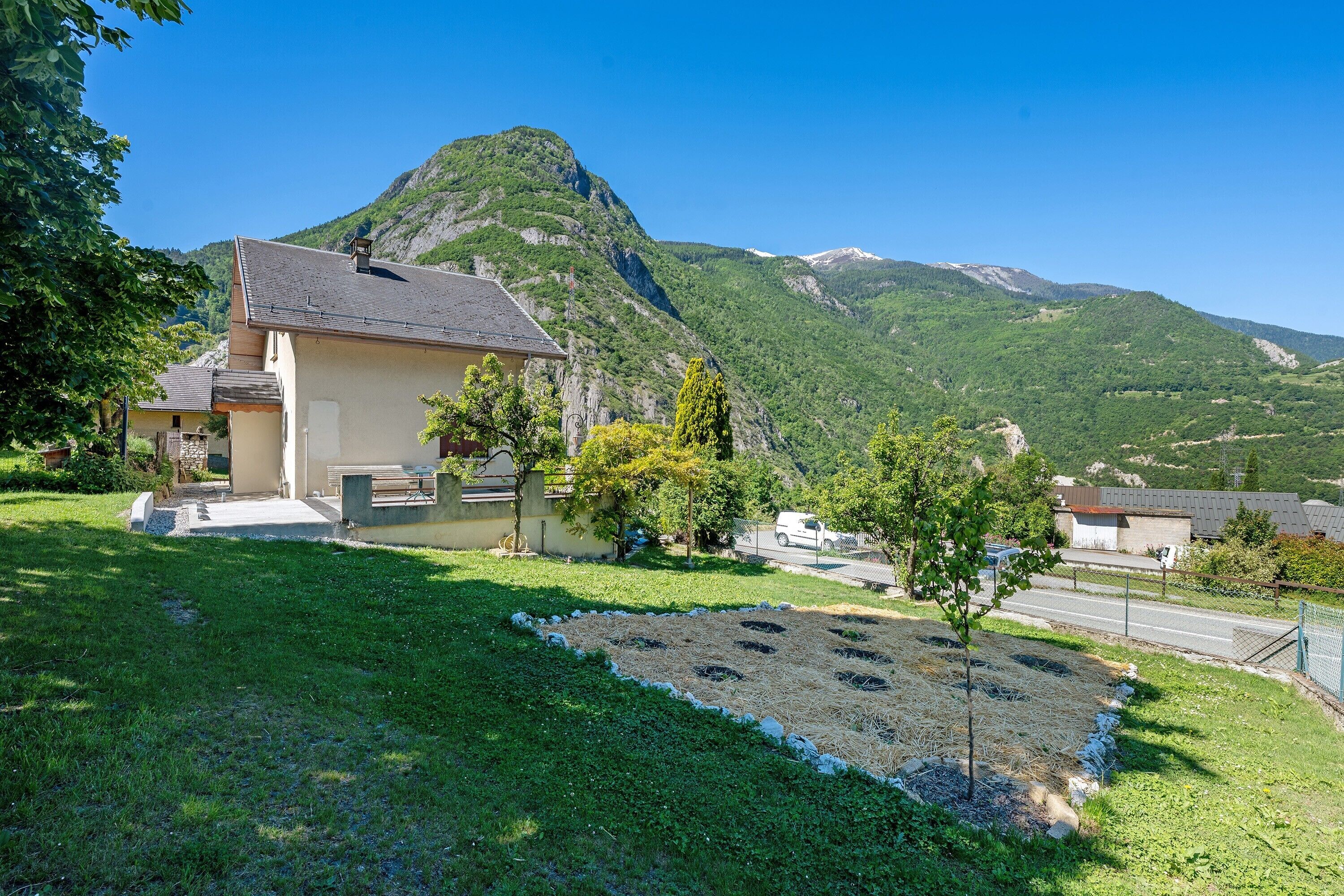A house with a sloped roof, a paved driveway, and a grassy area with a circular pattern of holes.