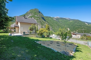 A house with a sloped roof, a paved driveway, and a grassy yard with a small tree.