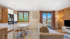 Ein modernes Wohnzimmer mit Sofa, einem Esstisch mit Stühlen, einem Fernseher und einer Küchenzeile mit Geräten.