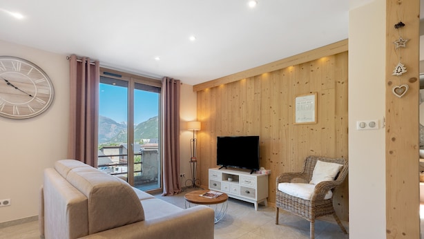 Ein modernes Wohnzimmer mit einer Couch, einem Korbsessel, einem Fernseher und einer Holzwand.