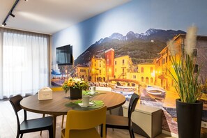 Zona pranzo con tavolo apparecchiato per due, kit di benvenuto e pianta in vaso.