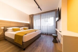 Une chambre d’hôtel moderne, équipée d’un lit, d’une table de chevet, d’un téléviseur fixé au mur et d’une fenêtre avec des rideaux.