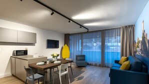 A modern living room with a dining area, a sofa, a chair, a TV, and a kitchen area with a microwave. - Apartment 'Boutique Yellow' with Balcony, Wi-Fi and Air Conditioning (Nago-Torbole)