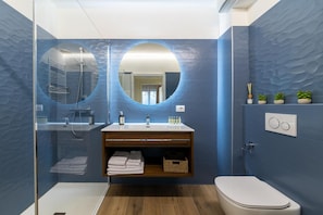 Un bagno moderno con cabina doccia in vetro, uno specchio rotondo, un lavandino bianco e un water.