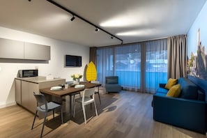 Un soggiorno moderno con angolo da pranzo, un divano, una poltrona, una televisione e un'area cucina con forno a microonde.