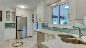 A modern kitchen with white cabinets, a stainless steel refrigerator, a sink, and a window with a view of greenery outside. - Peaceful Lakeside Escape• Trails & Parks Nearby (Grimsby)